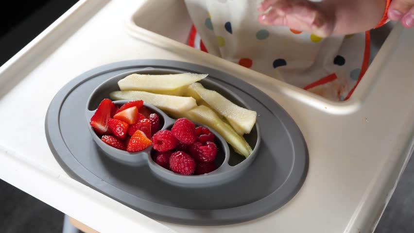 Baby taking fruit pieces from a grey silicone plate, baby led weaning