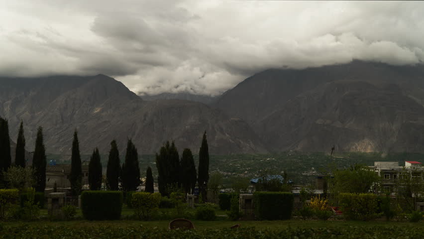A captivating time-lapse video capturing fast-moving clouds over the mountains of Pakistan, with pine trees in the foreground and golden sunlight piercing through the peaks.