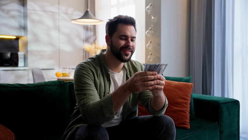 Happy rich wealthy Caucasian man business male businessman guy homeowner counting money dollars cash salary bank winning getting wages betting wealth gambling richness accounting at home living room
