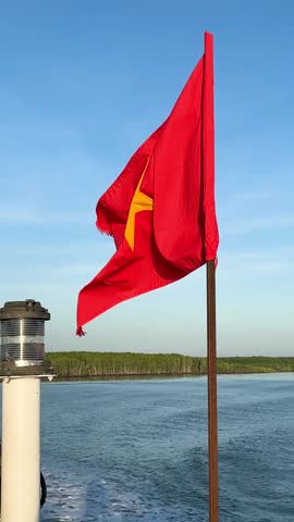Vietnam flag waving flying on blue sky from boat deck with ocean view, vertical video. beautiful vietnamese flag on 50 years celebration liberty day
