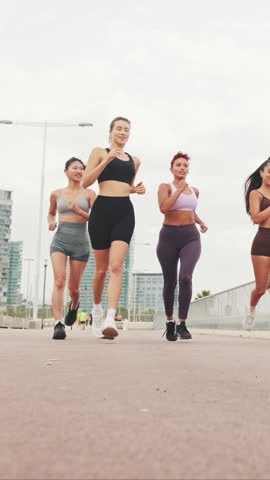 Vertical video, Four young women running in the city. They are wearing sports bras and shorts. Urban fitness and healthy lifestyle.