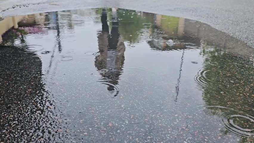 Close up slow motion shot of legs in white sneakers stepping into muddy puddle. Sad woman walking in rain, making splash.
