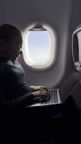 Redhead woman flying in airplane cabin working remotely on laptop with coffee in hand pausing to look out bright window moment of digital clarity calm routine in summer journey and focused tech