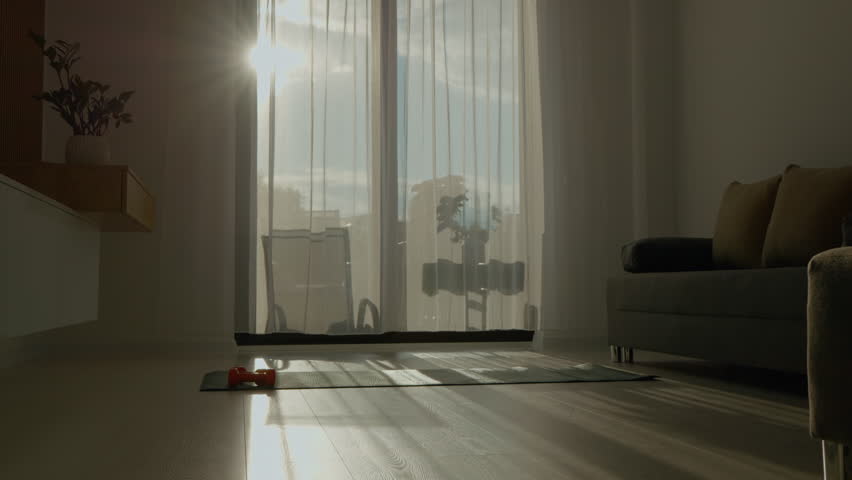 Morning sunlight streams through sheer curtains into a peaceful living room featuring a sports mat and dumbbells, creating an inviting space for home workouts.