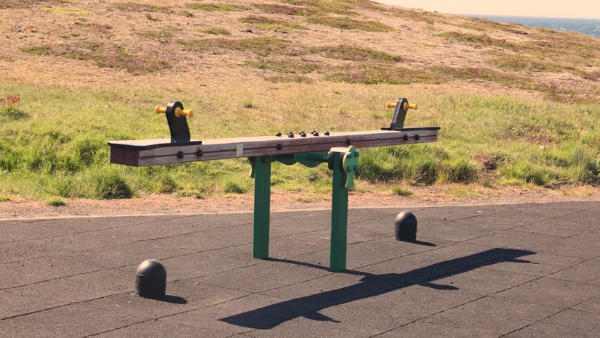 An empty seesaw swing gently moving in the breeze on a grassy green hillside. Surrounded by quiet nature and light fog, evoking childhood memories and peaceful solitude.