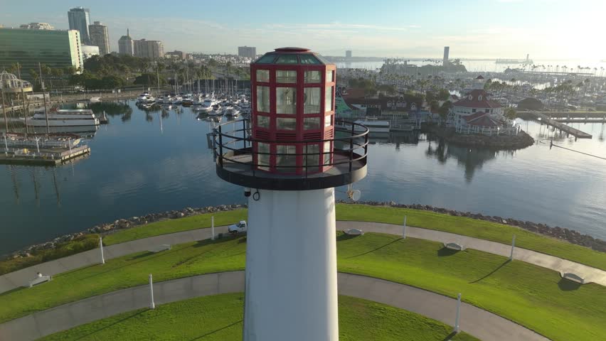 Aerial establishing shot of Lions Lighthouse at Shoreline Park in Long Beach, California, as dawn lights up the peaceful harbor and stunning skyline.
