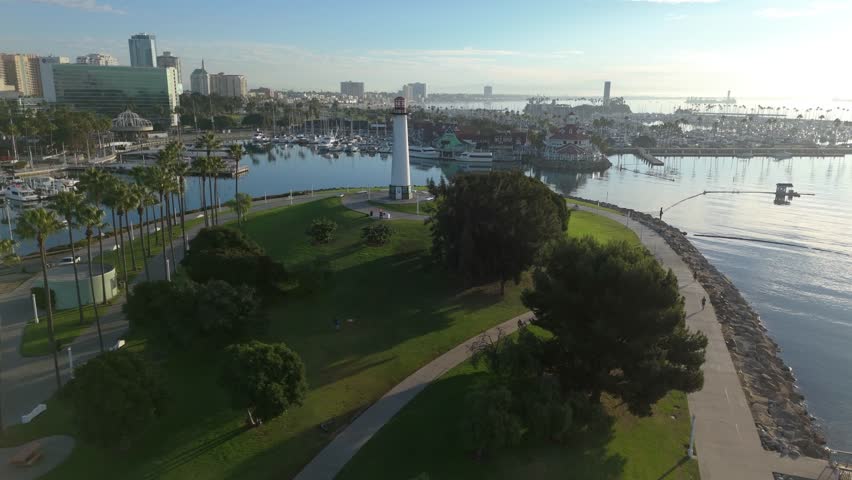 Aerial orbit shot of Lions Lighthouse and Shoreline Aquatic Park at dawn, revealing marina and stunning cityscape in Long Beach, California.