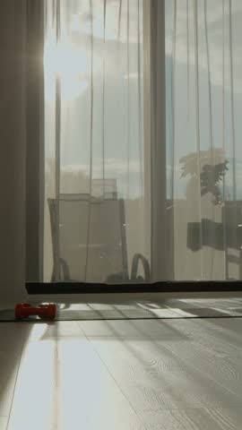 Vertical Screen: Morning light streams through sheer curtains, illuminating a peaceful living room. A sports mat and dumbbells sit ready for a refreshing workout at home.