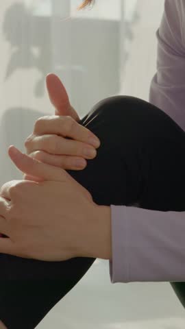 Vertical Screen: A woman performs exercises in her living room despite experiencing knee pain. She adjusts her position to manage her discomfort while staying active.