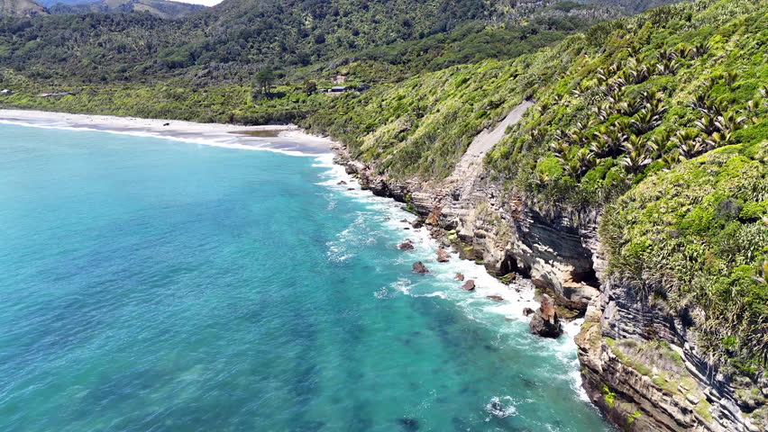 Aerial view of rocky coastal landscape with waves and lush greenery, West Coast of New Zealand. 