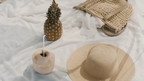 Flat lay of tropical summer essentials featuring a fresh pineapple, coconut drink with a straw, straw hat, and woven bag on a white blanket, ideal for travel promos.  - Powered by Shutterstock - Get 15% off with code: PIKWIZARD15