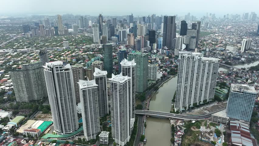 Manila cityscape at river banks aerial. Downtown area with cottages, skyscrapers, buildings. Urban Philippines city scape with streets and roads. Town drone shot. Poor Homes Along Rich Skyscrapers.