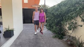 Couple in their late 50s walking arm in arm through a cobblestone alley, dressed in summer sportswear and enjoying a quiet moment in a charming urban setting - Powered by Shutterstock - Get 15% off with code: PIKWIZARD15