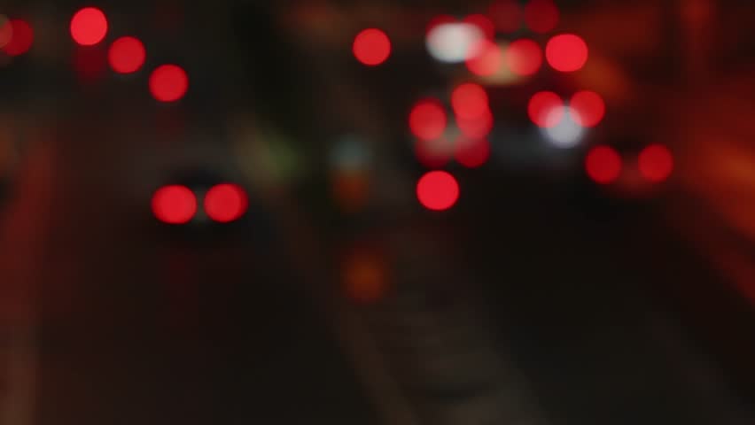 Abstract view of blurred red tail lights from moving traffic on a night city road. Soft bokeh effect against a dark urban background