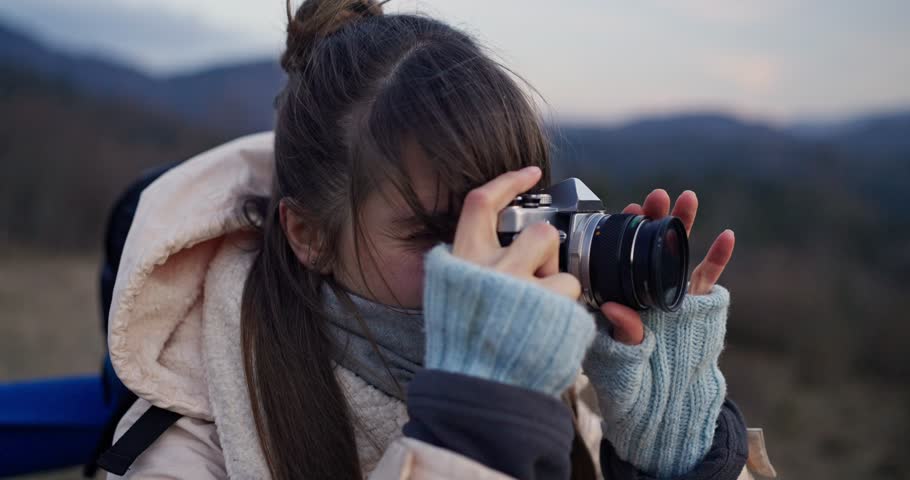 Close up of happy girl in hiking clothes taking a picture of the view with her camera during a hike in the mountains and forests