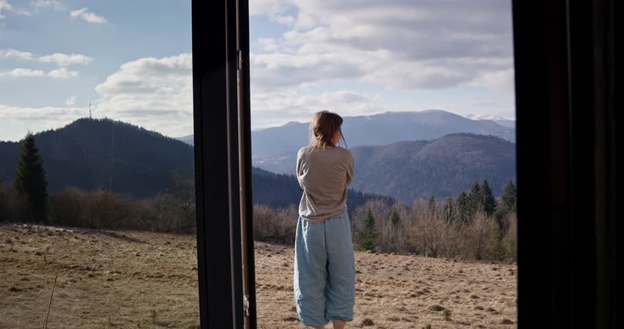 Zoom in girl stands with her back and looks at the mountain landscape during her morning in a non-urban area. Enjoying the beauty of nature and mountains
