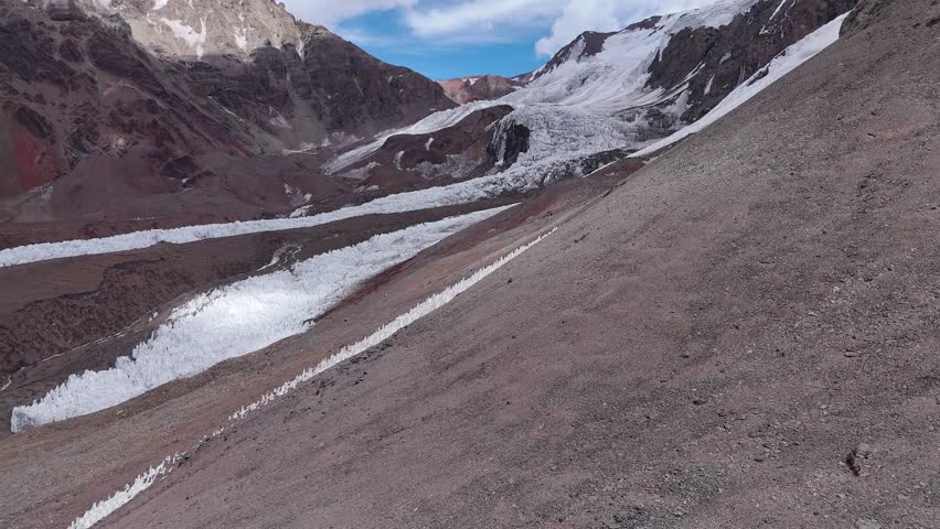 Aerial view of a glacier on Aconcagua, Argentina. The icy formations contrast with the barren, rocky Andean landscape. High-altitude terrain dominates the background