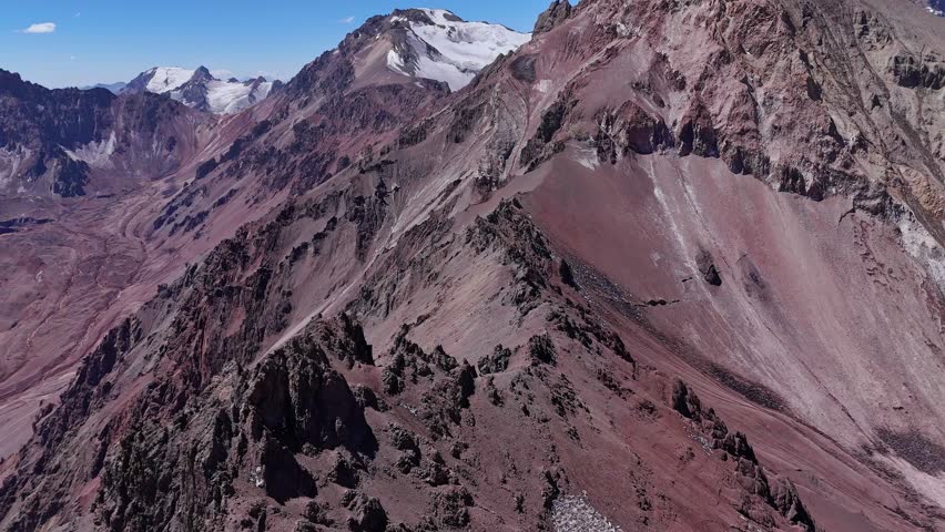 Aerial view of rugged Andes mountains near Aconcagua, Argentina. Steep ridges, rocky terrain, and patches of snow dominate the high-altitude landscape.