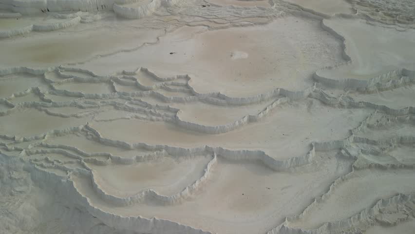 Drone glides over Pamukkale's stunning white limestone pools. Fields surround the travertine in Turkiye. Aerial view captures natural beauty of Turkish thermal site.