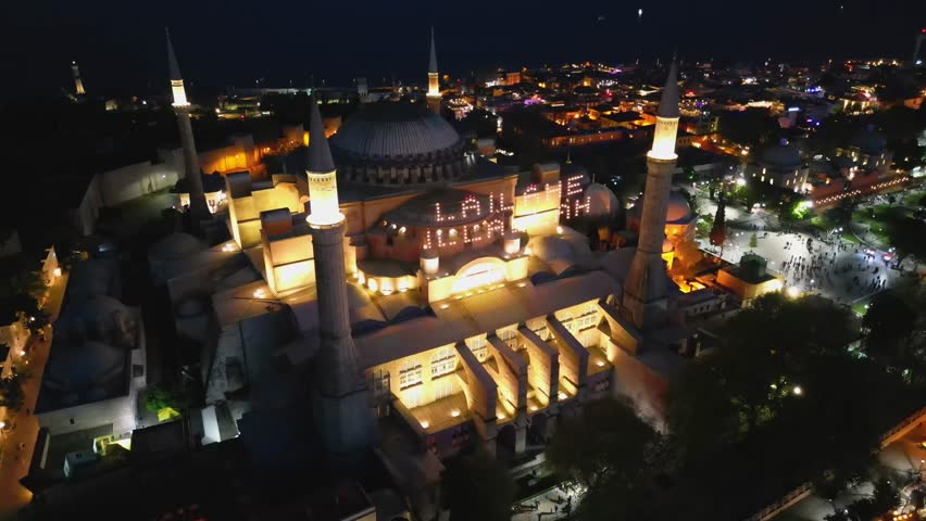 Stunning nighttime aerial view of Hagia Sophia in Istanbul, Turkey. Ancient architectural marvel lit warmly, surrounded by the city lights. Captures spiritual and historic depth.