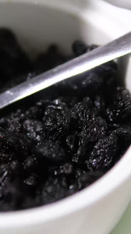 Black raisins slowly rotating in wooden bowl. Dried grapes close up. Dried fruits and dry berries