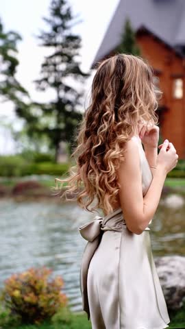 A girl in a dress with a bare back on the street near the lake with her back turned with beautiful curly hair