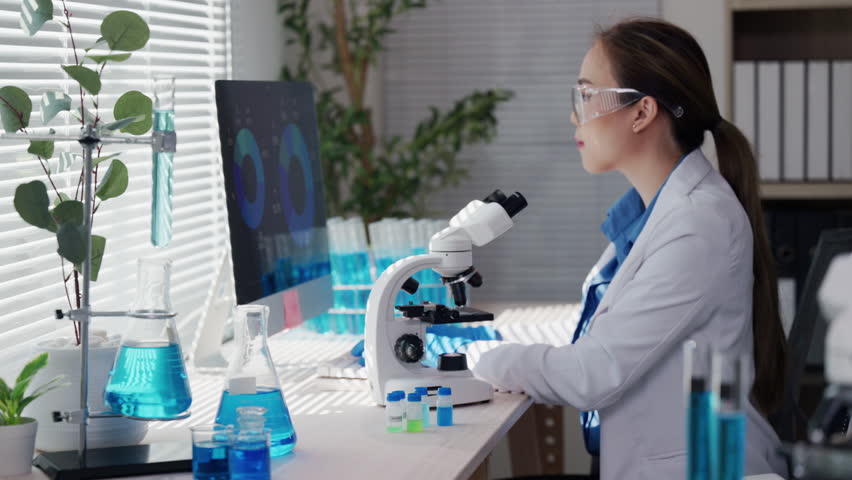 Female scientist wearing lab coat and safety glasses carefully analyzing scientific samples under microscope, focusing on precise research details in modern laboratory setting - Powered by Shutterstock - Get 15% off with code: PIKWIZARD15