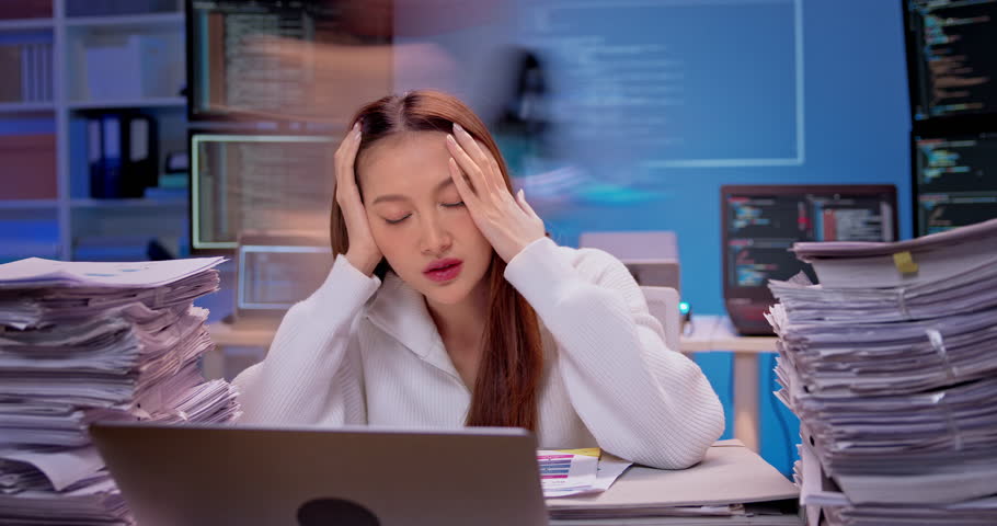 Asian businesswoman working overtime at modern office desk. Piles of paperwork grow rapidly as colleagues rush past. pressure and work overload. Time lapse young woman works late at night. Fast speed.