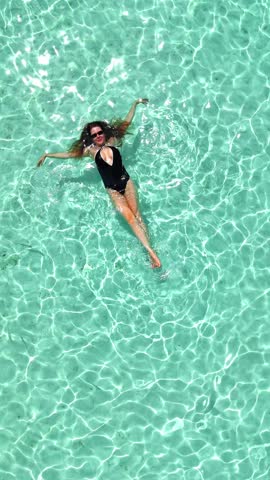 Woman floating in crystal clear turquoise water, arms stretched, enjoying relaxation on tropical island, peaceful leisure moment, travel, summer vacation, hotel promo, Maldives