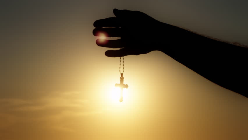 Male Hand is Holding Christianity Religion Symbol Cross in Sunset Light Near the Seaside