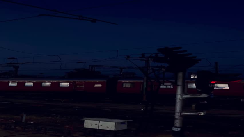 A cinematic early morning scene at an Indian railway station featuring a red passenger train passing under electric lines, shot during dawn with visible moonlight and platform lighting.
