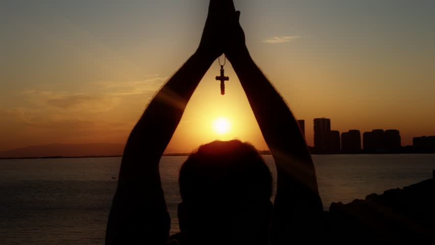 Male Hand is Holding Christianity Religion Symbol Cross in Sunset Light Near the Seaside