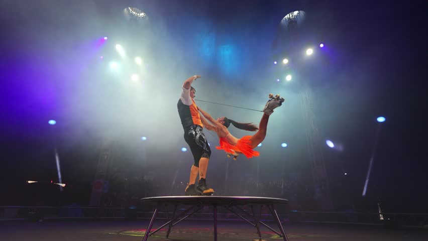 Young pair of acrobats, man and woman, on roller skates perform in a circus on a small round stage