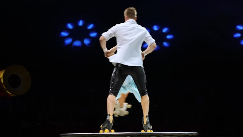 Young pair of acrobats, man and woman, on roller skates perform in a circus on a small round stage