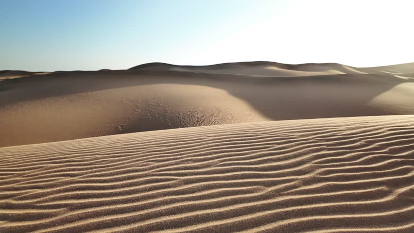 Gradual footprints emerging across golden sand dunes, revealing windswept desert landscape with serene slow motion progression through arid wilderness terrain