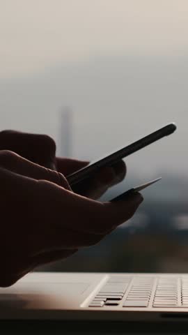 Female hands with credit debit card and cellphone shopping online entering digits and cvv code with laptop computer. Vertical video
