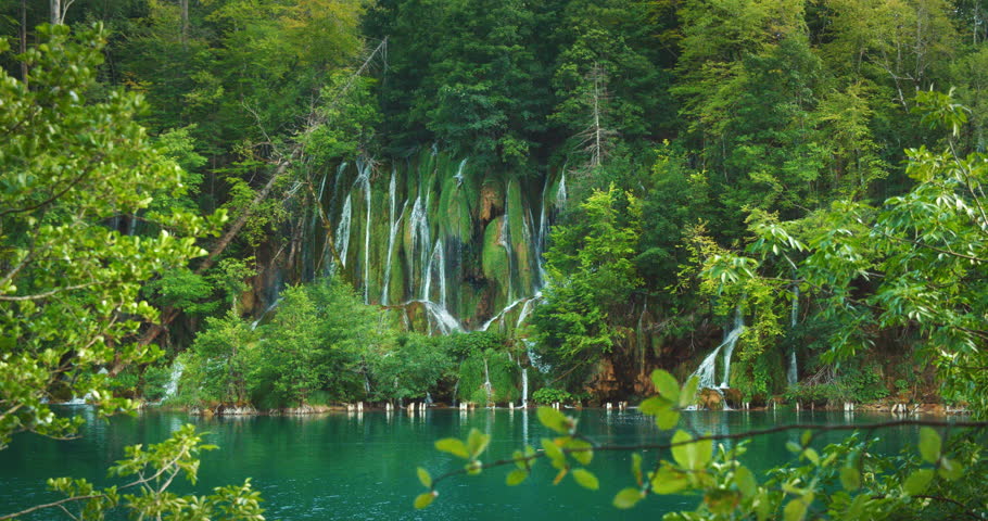 Moss-covered cliffs with multiple waterfalls cascading into emerald lake in Plitvice Lakes Croatia