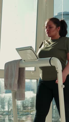 Woman is walking on treadmill at home. Female is exercising on treadmill in the morning. Vertical video