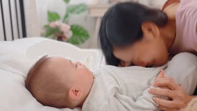 Asian single mother lovingly cares for and raises her baby boy at home. Attractive mother shares a tender moment playing with her newborn baby on bed in cozy bedroom, creating warm family environment. - Powered by Shutterstock - Get 15% off with code: PIKWIZARD15