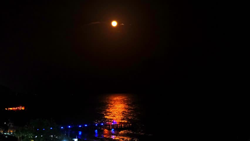 Moonlight Over Sea Waves Full Moon Glow ocean waves on sandy beach at night wooden pier. The moon illuminates water surface. Concept of beach vacation slowing down on seacoast