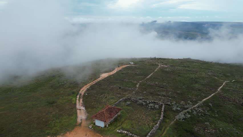 Ascending through cloud, aerial looks onto remote, old stone homestead