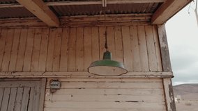 Old wooden shack with peeling paint. A green vintage lamp hangs from the ceiling. The corrugated roof provides shade. The fuse box is visible on the wall. Desert landscape in the distance. - Powered by Shutterstock - Get 15% off with code: PIKWIZARD15