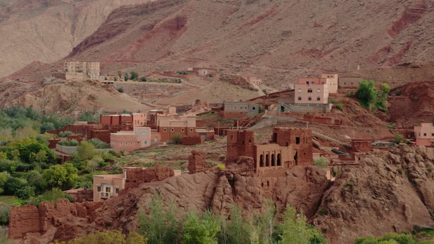 Traditional Moroccan village nestled in a valley of the Atlas Mountains. This stunning footage captures the essence of rural life in Morocco, with its red clay buildings, lush green oasis,