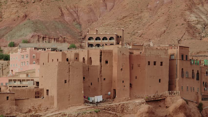 Traditional Moroccan village nestled against the Atlas Mountains. The buildings, constructed from adobe, blend into the landscape. This scene evokes a sense of history and timelessness.