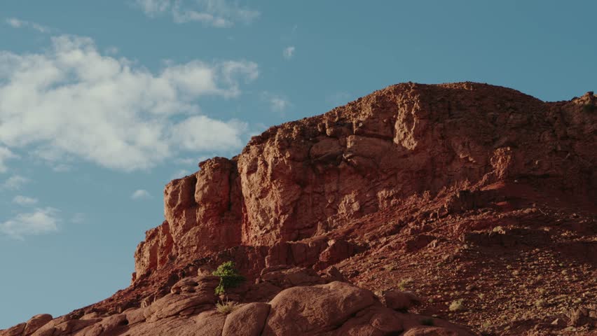 Majestic red rock formations in Morocco. The rugged landscape stretches under a clear blue sky, with sparse vegetation clinging to the slopes. adventure and exploration.