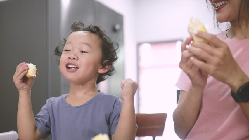 Asian mom and son sitting on the floor watching a tablet together. Cozy and candid vertical moment of digital bonding at home.