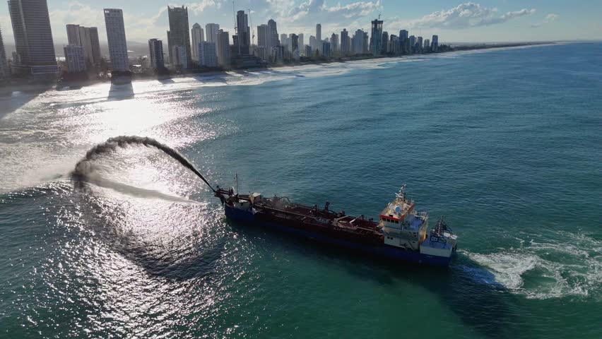 A dredging ship pumps sand to restore beach erosion along the Gold Coast, captured in bright daylight with city skyline