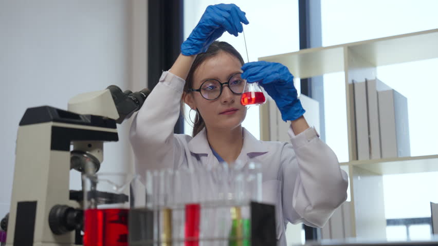 Female scientist in lab coat conducts precise experiments with test tube, showcasing focus and curiosity in vibrant laboratory filled with colorful liquids and advanced research tools. - Powered by Shutterstock - Get 15% off with code: PIKWIZARD15