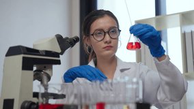 Scientist in lab coat conducts meticulous analysis of red liquid in test tube, showcasing precision and focus in laboratory research and experiment with microscope and gloves. - Powered by Shutterstock - Get 15% off with code: PIKWIZARD15