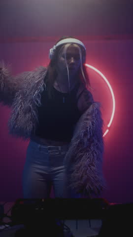 DJ stylish woman dancing on night rave in club performing at mixer controller. Female disk jockey wear fur coat playing modern electronic techno music set at party. Neon Lights, audio sound stage